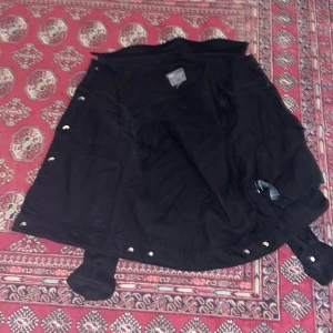 Svart jeansjacka från ASOS - Säljer en svart jeansjacka från ASOS i storlek M. Jackan har knappar framtill och två bröstfickor med lock. Perfekt för en cool och avslappnad stil.