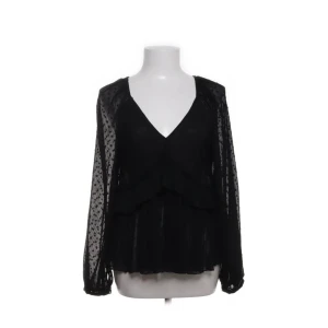 Svart blus med volanger  - Elegant svart blus med v-ringning. Blusen har ett diskret prickigt mönster och en lätt volangdetalj vid nederkanten. Den kommer från zara i storlek S
