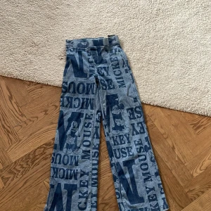 Blå jeansbyxor med Mickey Mouse-mönster från H&M - Snygga blå jeansbyxor från H&M med ett coolt Mickey Mouse-mönster. Byxorna har en rak passform och är perfekta för barn som älskar Disney. De är tillverkade i ett bekvämt denimtyg och har klassiska fickor.Och har inte riktigt fickor fram