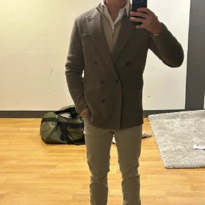 Beige kavaj - Snygg beige kavaj med dubbelknäppning och klassisk design. Perfekt för en stilren look. Kavajen har fickor fram och en elegant passform.