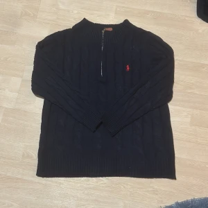 Mörkblå stickad tröja från Polo Ralph Lauren - Säljer en stilren svart stickad tröja från Polo Ralph Lauren med en dragkedja vid halsen och det klassiska röda logotypbroderiet på bröstet cable knit. Lite tunnar med original påse och prislappar. Fick den som en julklapp men var lite stor för mig. Den är S/M