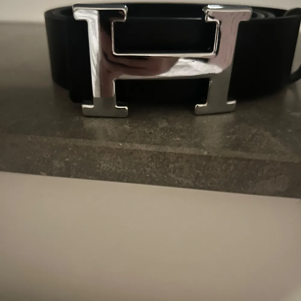 Stilrent svart bälte med ett iögonfallande silverfärgat H-spänne. Perfekt för att ge en elegant touch till din outfit. Passar bra till både jeans och kostymbyxor.. Muu.