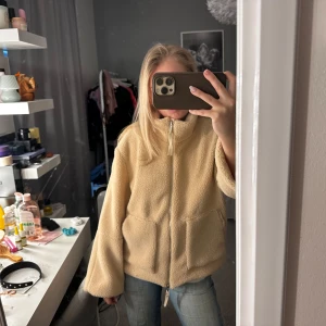 Rosa/beige teddyjacka med dragkedja - Mysig beige teddyjacka med dragkedja framtill. Jackan har en hög krage och stora fickor, perfekt för kyliga dagar. Den är långärmad och har en avslappnad passform som ger en bekväm känsla. Storlek s men mer xs skulle jag säga , väldigt lik den populära hm teddy jackan