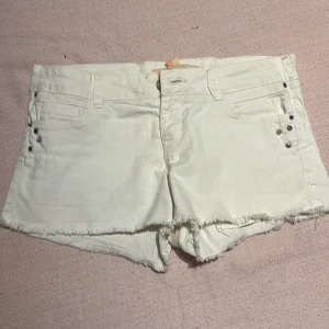 Vita shorts från Bershka - Snygga vita shorts från Bershka med fransiga kanter och nitar vid fickorna. De har en klassisk femficksdesign och knappgylf. Knappt använda och i väldigt bra skick!🌺