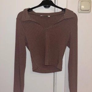 Brun ribbad topp - Snygg brun ribbad topp från Asos med v-ringning och krage, croppad design. Endast testad, strl 32.