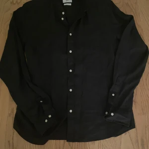 Svart skjorta från Bläck - Snygg svart skjorta från Bläck i storlek M. Skjortan har en skräddarsydd passform med långa ärmar och klassiska knappar framtill. Perfekt för en stilren look.