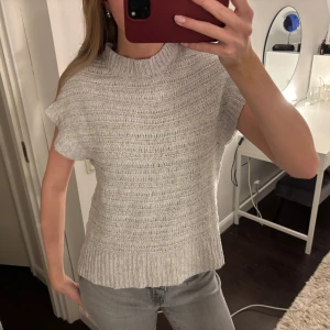 Grå stickad topp - Säljer en stilren grå stickad topp med korta ärmar och ribbad struktur. Perfekt för en avslappnad men ändå elegant look. Passar bra till jeans eller kjol. Hör av dig vid intresse!