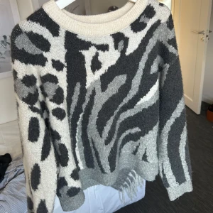 Grå och vit mönstrad tröja från Vero Moda - Säljer en snygg grå och vit tröja från Vero Moda med ett djärvt mönster. Tröjan har långa ärmar och en rund halsringning. Perfekt för att ge din outfit en cool touch.