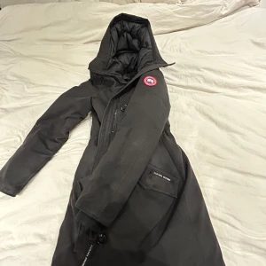 Svart dunjacka- Canada Goose - Säljer en svart dunjacka från Canada Goose med huva och dragkedja (päls till huvan finns).                        Jackan har används varsamt och endast tagits fram under två vintrar! Inga som helst fel på den:).        Jackan är i storlek L och kan justeras med hjälp av ”gummibanden” på insidan, funkar bra för mig i storlek M😊