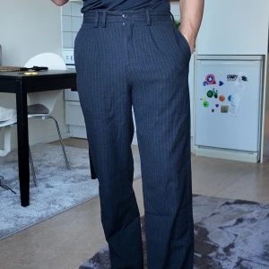 Mörkblå randiga kostymbyxor från Zara -  mörkblå kostymbyxor från Zara med  ränder. Byxorna har en klassisk passform med dragkedja och knappar i midjan. Storlek 36 