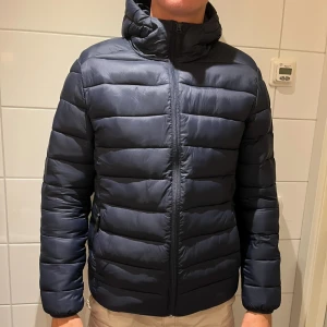 Mörkblå vinterjacka  - Mörkblå vinterjacka från lindbergh i herrstorlek M. En söm som har gått upp på luvan vilket man ser på bild 3, annars väldigt fint skick. Säljer för 400 kr. 