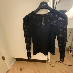 Svart spetsblus från Gina Tricot  - Elegant svart spetsblus från Gina tricot med långa ärmar och ett delikat spetsmönster. Perfekt för en stilren look.