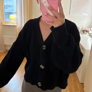 Svart kofta med stora knappar - Säljer en svart kofta med stora knappar framtill. Koftan har en loose passform och långa ärmar, perfekt för kyligare dagar. Den är stickad och ger en mysig känsla. Passar bra till både jeans och kjol.