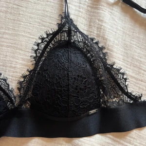 Svart spets bralette - Snygg svart bralette i spets. Den har justerbara axelband och en elegant spetsdesign som ger en lyxig känsla. Perfekt för att lägga till en touch av elegans till din outfit.