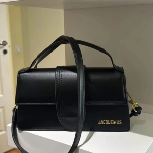 Svart handväska från Jacquemus - Snygg svart handväska från Jacquemus i skinn. Väskan har en stilren design med ett justerbart axelband och en elegant stängning framtill. Perfekt för att ge din outfit en lyxig touch.