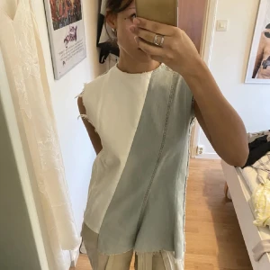 Ärmlös topp i denim och vitt tyg - Säljer en unik ärmlös topp med en kombination av denim och vitt tyg. Toppen har råa kanter och en asymmetrisk design som ger en cool och avslappnad look. Perfekt för en trendig stil.
