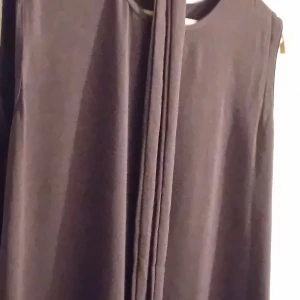 Mörkbrun långklänning+lång jacka - Elegant mörkbrun långklänning i ett mjukt och flödande material. Klänningen är ärmlös och har en stilren design som passar perfekt för höst- och vinterfester. Den långa längden ger en sofistikerad look.