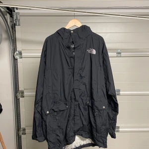 Svart regnjacka från The North Face - Säljer en svart regnjacka från The North Face i bra skick. Jackan har en justerbar huva och långa ärmar, perfekt för regniga dagar. Den är tillverkad i ett lätt och slitstarkt material med The North Face-logga på bröstet. Passar både för vardag och utomhusaktiviteter. Säljes i befintligt skick. Storlek: XXL