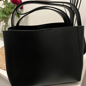 Svart PU axelväska - Snygg och stilren svart axelväska i PU-material. Perfekt för vardagsbruk🥰 Väskan har en minimalistisk design som passar till alla olika outfits. Den är helt ny & oanvänd! Köpt för 299 kr, men säljer den för 150 kr! 