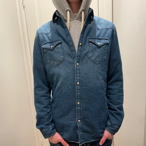 Blå jeansskjorta från Selected Homme med tryckknappar - Snygg blå jeansskjorta med tryckknappar och två bröstfickor. Perfekt för en avslappnad stil. Skjortan har långa ärmar och en klassisk krage. PRIS KAN DISKUTERAS!
