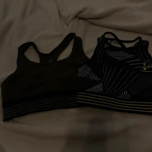 Två sport-bh:ar från H&M och Craft - Säljer två sport-bh:ar i storlek Xs. Den ena är från H&M i en mörkgrön nyans med svarta ränder. Den andra är från Craft med ett svartvitt geometriskt mönster och gula detaljer. Perfekta för träning och ger bra stöd.🖤