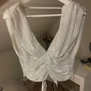 Fin glittrig nyårs topp - Snygg vit glittrig topp med knytning i midjan och djup v-ringning. Perfekt för festliga tillfällen så som nyår