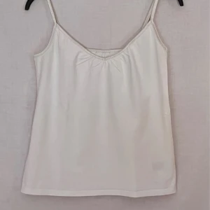 Vit linnetopp - Säljer en enkel och stilren vit linnetopp i bomull och elastan. Perfekt för sommardagar eller som ett basplagg i garderoben. Den har smala axelband och en bekväm passform. Lite nopprig på insidan 