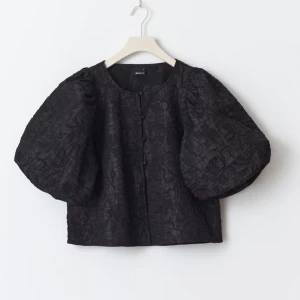 Svart blus med puffärmar - Säljer en elegant svart blus med stora puffärmar och knappar framtill. Perfekt för en stilren look, oavsett om det är till vardags eller fest. Materialet har en lätt glansig yta som ger en lyxig känsla. Passar bra till både jeans och kjol! Nypris 500kr