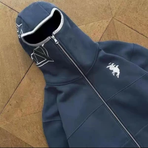 Mörkblå hoodie med dragkedja - Säljer en mörkblå hoodie med dragkedja och ett coolt tryck på bröstet. Perfekt för höst och vinter, den är både stilren och bekväm. Huvan har en unik design med vita detaljer. Passar perfekt för en avslappnad stil.