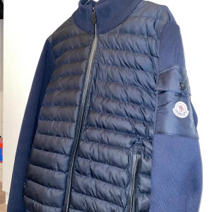 Mörkblå jacka från Moncler - Säljer en snygg mörkblå jacka från Moncler i mycket bra skick. Jackan har en quiltad design med dragkedja framtill och ribbstickade detaljer vid kragen och ärmsluten. Perfekt för höst och vår! 🧥