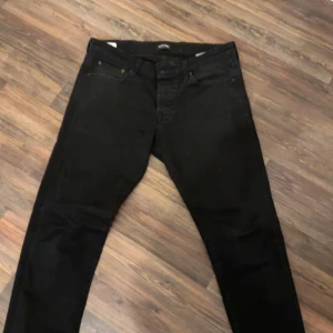 Svarta jeans från Jack & Jones - Säljer ett par svarta superstretch jeans från Jack & Jones. De har en klassisk design med fem fickor och knappgylf. Perfekta för en bekväm och stilren look.