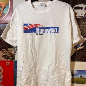 Vit t-shirt från Hanes med tryck - Vit t-shirt från Hanes med tryck 'Charles E. Kurowski For Judge' i blått och rött. T-shirten har en klassisk passform. Finns tyvärr en rosa fläck på baksidan som man ser på sista bilden. Syns dock ej under användning. Dm vid frågor.