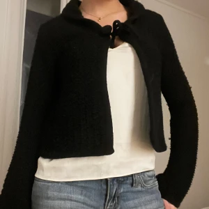 Svart stickad kofta - Säljer en svart stickad kofta med knytning framtill. Koftan har långa ärmar och en croppad passform, perfekt för lager på lager-stil. Enkel och stilren design som passar till många olika outfits. Pris går att diskutera✨