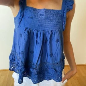 Blå ärmlös topp med volangdetaljer från mango  - Säljer en superfin blå ärmlös topp med volangdetaljer och broderade blommor. Perfekt för sommardagar! Den har en luftig passform och är gjord i ett lätt och bekvämt material. Toppen är i mycket bra skick och redo för nya äventyr. Passar perfekt till jeans eller shorts!