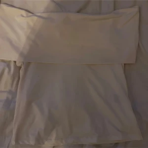 Vit offshoulder topp - Säljer en stilren vit offshoulder topp i storlek M. Perfekt för sommardagar eller en kväll ute. Toppen är enkel men elegant och kan matchas med både jeans och kjol för en chic look.