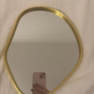 Oregelbunden spegel med guldram - Säljer en unik spegel med oregelbunden form och en elegant guldram. Perfekt för att ge ditt rum en modern och stilren touch. Spegeln är i mycket bra skick och kan enkelt hängas upp på väggen. Passar både i hallen och sovrummet för en chic look. Aldrig använd. Pris kan diskuteras! 