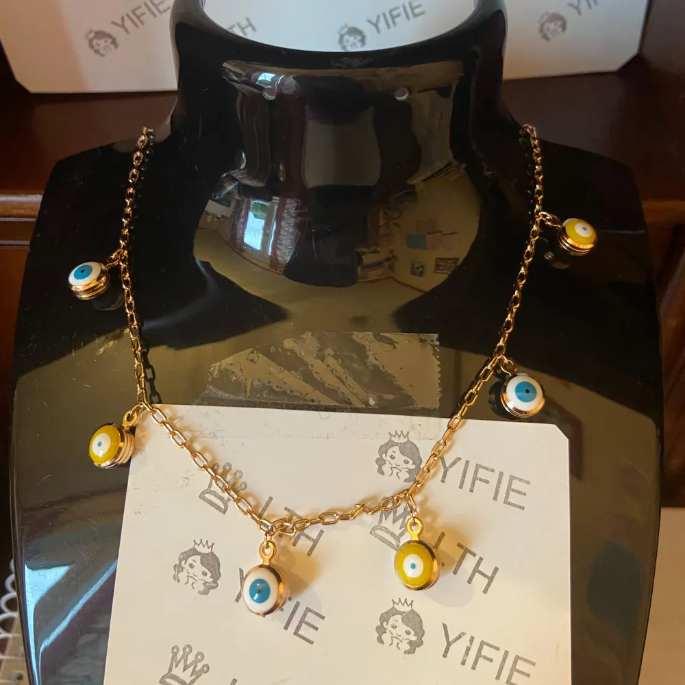 Snyggt set med halsband och örhĂ€ngen. Halsbandet har en kedja i rusaguld med hĂ€ngande Ă€kta 𧿠ögonmotiv i blĂ„tt och gult. ĂrhĂ€ngena matchar med samma ögonmotiv. Perfekt för att ge en unik touch till din stil.. Asusteet.