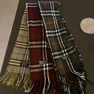 Rutig halsduk från Burberry - Säljer tre stiliga rutiga halsdukar från Burberry i olika färger: grå, vinröd och mörkgrön. Tillverkade i mjuk ull med klassiskt rutmönster och fransar i ändarna. Perfekta för att hålla dig varm och snygg under kyliga dagar.   Säljer alla 3 för 1000kr eller 1st för 400