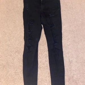 Svarta jeans med hål - Svarta jeans med hål på båda benen längs överbenet.