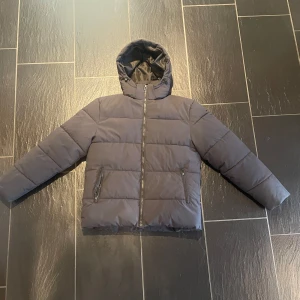 Svart pufferjacka från Studio Total - Säljer en snygg svart pufferjacka från Studio Total i storlek S. Jackan har en dragkedja framtill och en praktisk huva. Perfekt för kyliga dagar och håller dig varm och bekväm. Passar både till vardags och lite mer avslappnade tillfällen.                  Storleken är S men skulle mer säga M