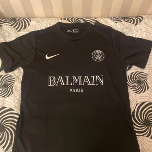 Svart PSG x Balmain fotbollströja - Säljer en svart PSG x Balmain fotbollströja i storlek M. Tröjan är i nytt skick med korta ärmar och har både Nike-loggan och Paris Saint-Germain-emblemet på bröstet. Perfekt för alla PSG-fans som vill ha något unikt och stilrent. 🖤