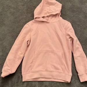 Rosa hoodie från lager 157 - Mysig rosa hoodie från lager 157 i storlek 140. Perfekt för kyliga dagar med sin mjuka och bekväma passform. Den har en klassisk känguruficka och en skön huva. Passar både till vardags och avslappnade tillfällen. 🩷