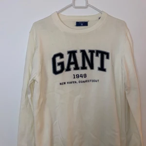 Vit tröja från GANT - Säljer en stilren vit tröja från GANT med tryck 'GANT 1949 New Haven, Connecticut' på bröstet. Tröjan är i bra skick och har en klassisk rund halsringning. Perfekt för en avslappnad och snygg look!