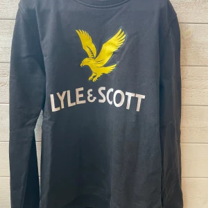 Svart långärmad tröja från Lyle & Scott - Säljer en svart långärmad tröja från Lyle & Scott med deras ikoniska gula örntryck på bröstet. Perfekt för både vardag och skola. Tröjan är i bra skick och gjord av mjukt bomullsmaterial. Passar perfekt till jeans eller chinos!