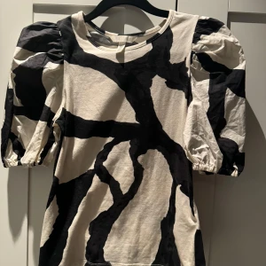 Svartvit mönstrad topp med puffärmar - Säljer en cool svartvit topp med ett unikt mönster. Den har puffiga trekvartsärmar som ger en trendig look. Perfekt för både vardag och fest!