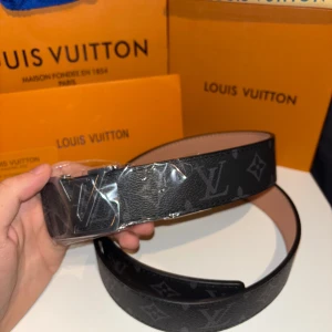 Svart bälte med monogram mönster  - Säljer snygga märkes bälten. Bältet har ett stort silverfärgat spänne som verkligen sticker ut. Perfekt för att ge din outfit en lyxig touch.  Passar både till vardag och fest! 