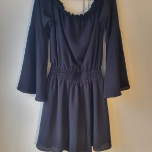 Svart klänning från NA-KD - Snygg svart klänning från NA-KD med lång ärm och elastisk midja. Perfekt för en stilren look med en bekväm passform. Klänningen har en enkel design som gör den lätt att matcha med olika accessoarer.