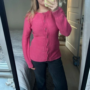 Rosa kofta med knappar - Säljer en söt rosa kofta med långa ärmar och knappar framtill. Koftan har en ribbad midja som ger en fin passform. Perfekt för att hålla sig varm och stilren.