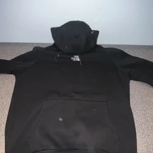 Svart hoodie från The North Face - Säljer en svart hoodie från The North Face med klassisk logga på bröstet. Perfekt för kyliga dagar med sin bekväma passform och praktiska huva. Ett måste i garderoben för alla som älskar stil och funktion.