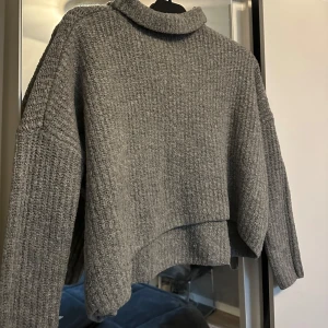 Grå stickad polotröja - Säljer en mysig grå stickad polotröja med ribbad struktur. Tröjan har långa ärmar och en avslappnad passform, perfekt för kyliga dagar. Den är både stilren och bekväm, ett måste i garderoben!